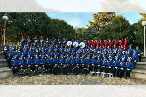 Large marching band in blue uniforms poses on outdoor steps with drums in front of them.